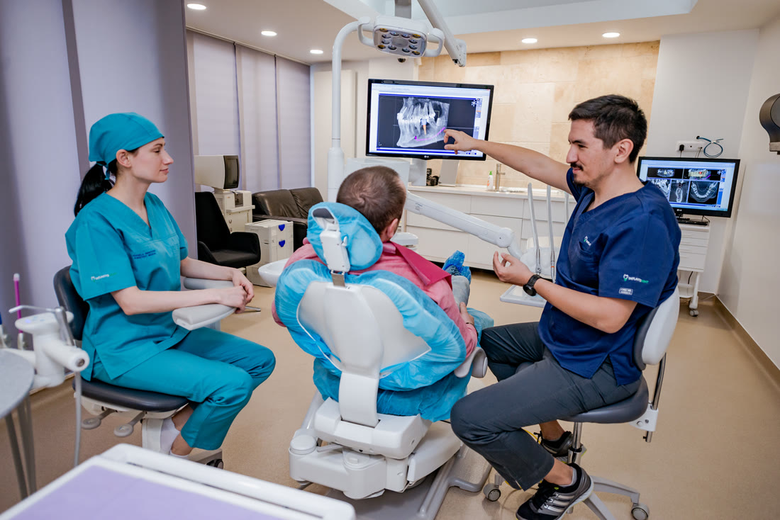 Medic Implantodent arată pacientului radiografia dentară pe monitor, în cabinet